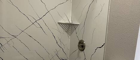 Une salle de bain comprenant des toilettes, une douche avec un pommeau de douche amovible et un mur orné d’un motif évoquant le marbre.