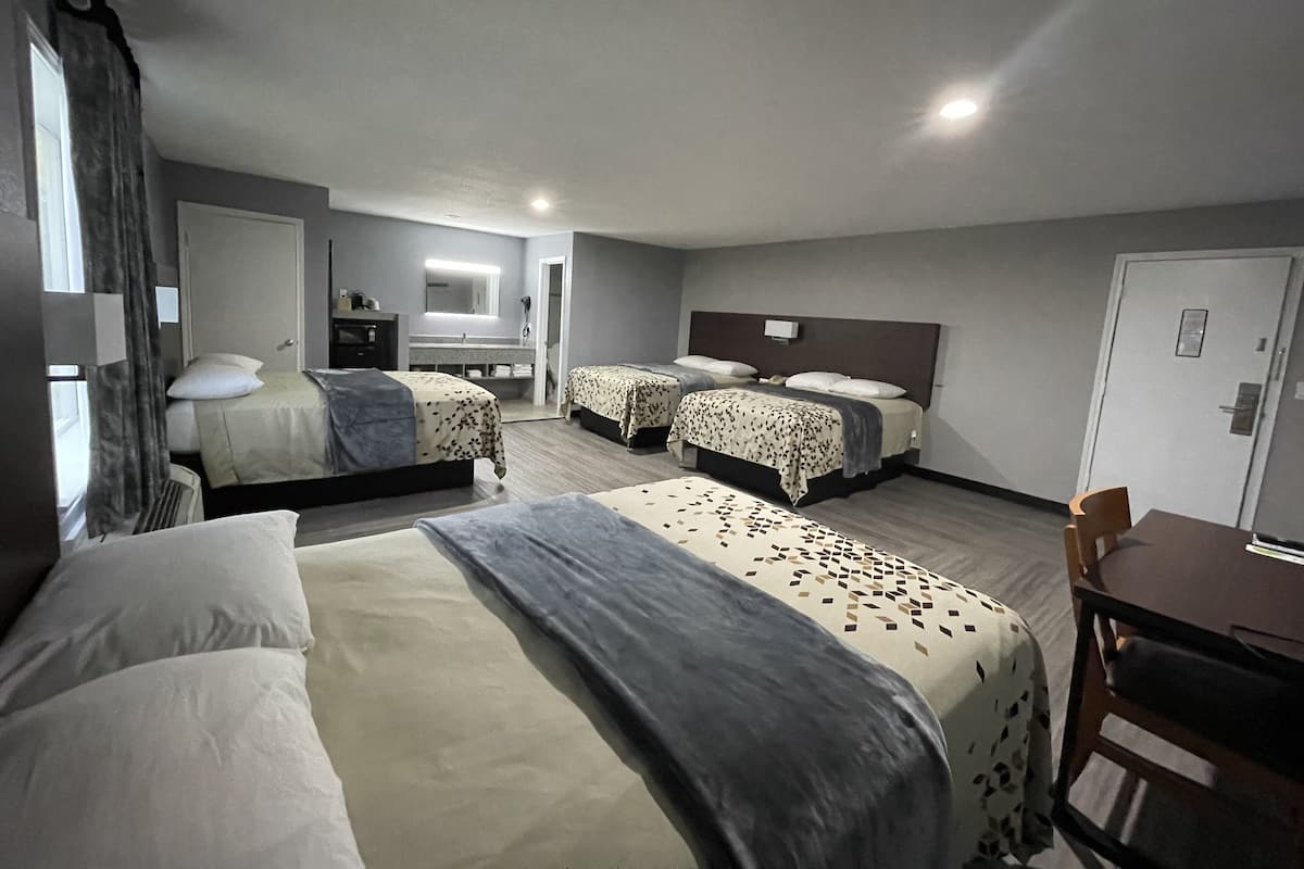 A hotel room with two beds, a desk, a chair, a bathroom, and a mirror.