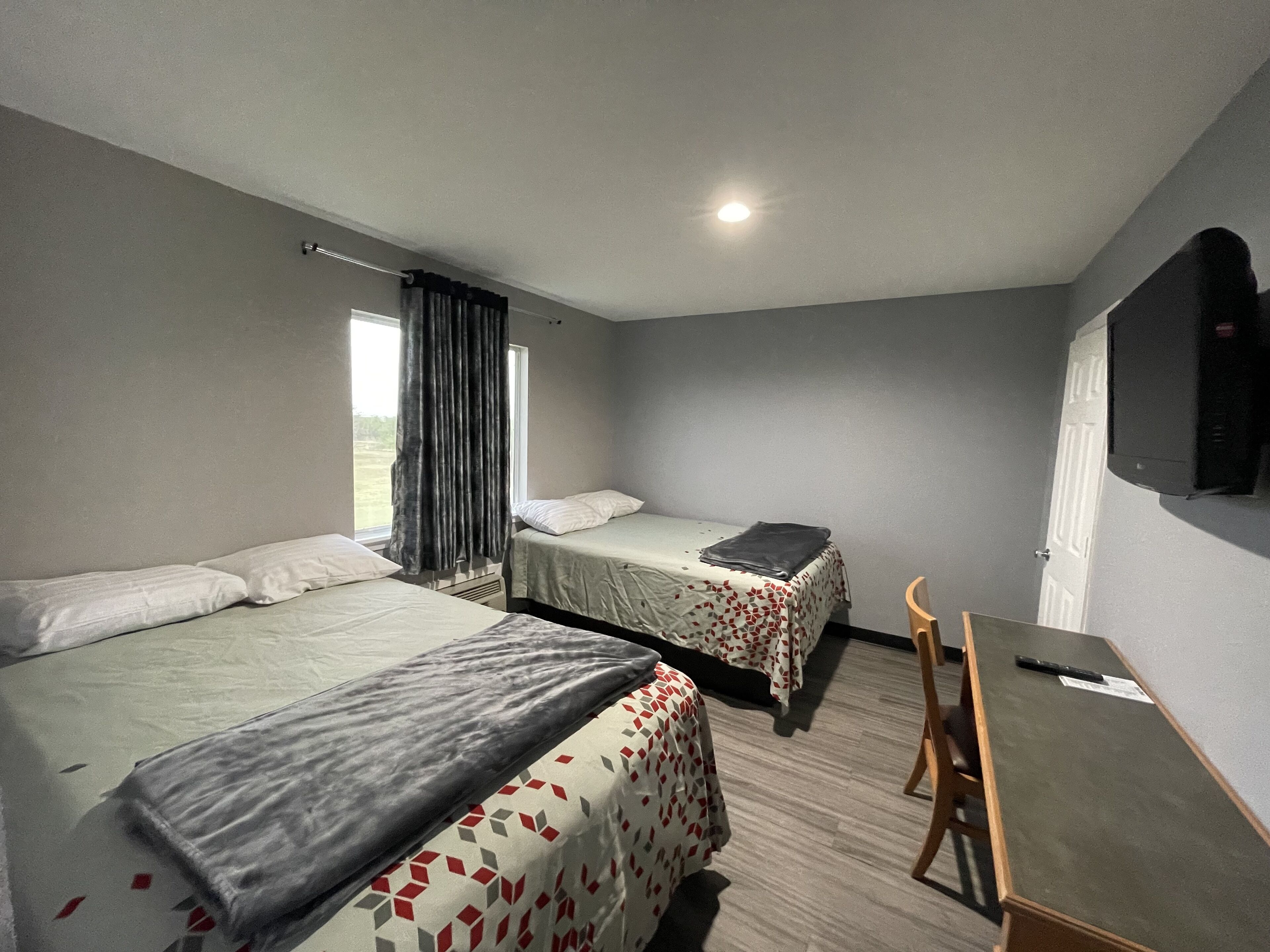 A hotel room with two beds, a desk, a chair, a TV, and a window with curtains.