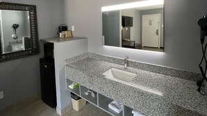 A modern bathroom with a granite countertop, a white sink, a large mirror, and a hairdryer on the wall.