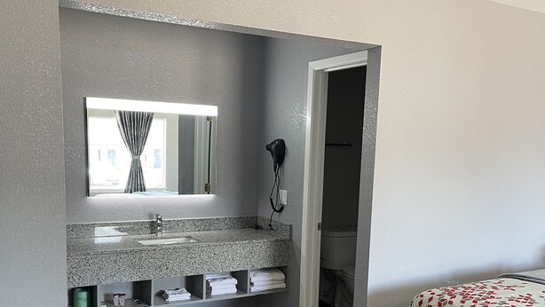 A bathroom with a granite countertop, a mirror, a hairdryer, and a toilet visible through an open door.