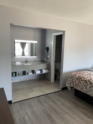 Un baño con encimera de granito, un espejo, un secador de pelo y un inodoro visible a través de una puerta abierta.