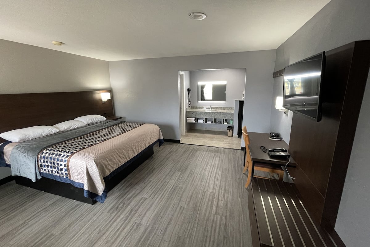 A hotel room with a bed, a desk with a telephone, a mirror, and a bathroom with a sink and mirror.