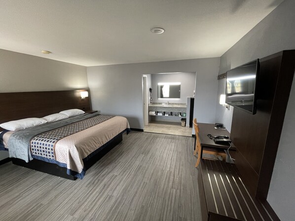 A hotel room with a bed, a desk with a telephone, a mirror, and a bathroom with a sink and mirror.