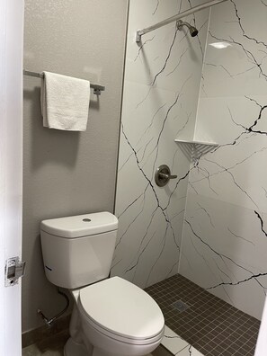 A bathroom with a toilet, a towel rack, a shower with a glass door, and a marble-patterned wall.
