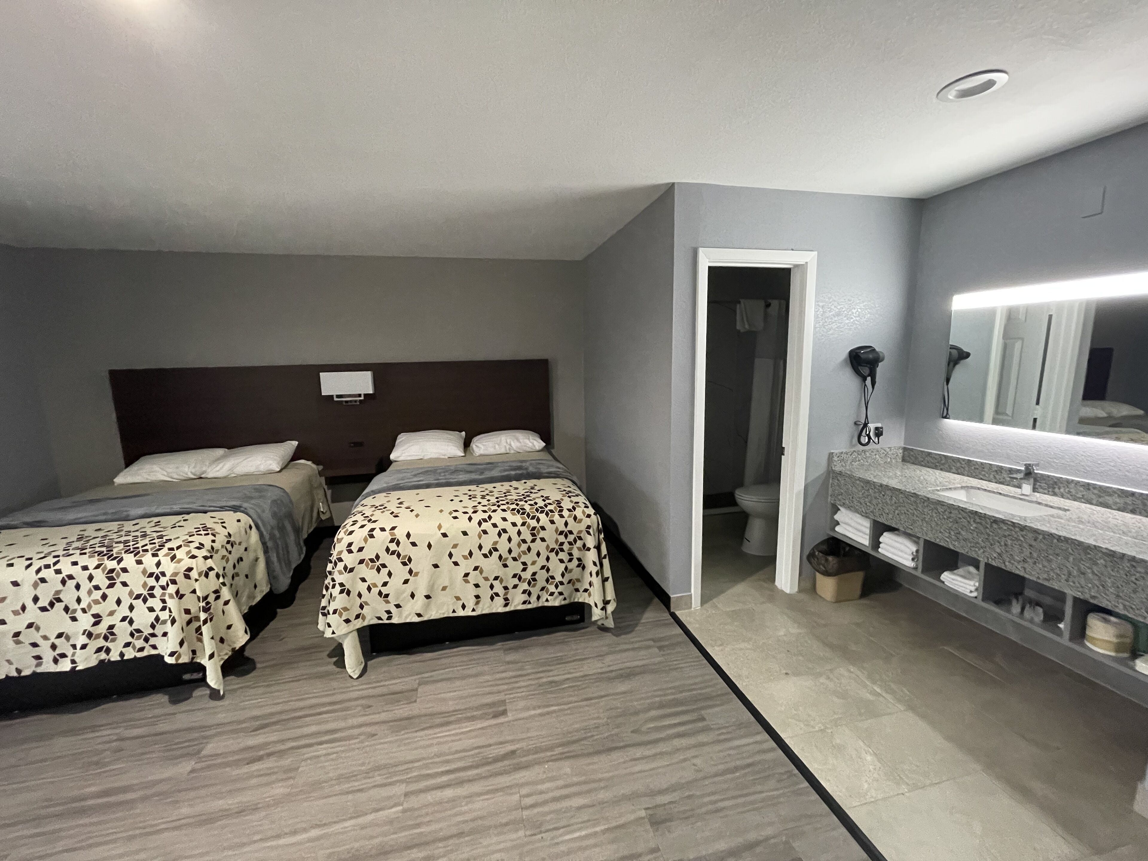 A hotel room with two beds, a bathroom with a sink and mirror, and a shower.