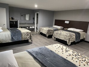 A hotel room with three beds, a bathroom with a sink and mirror, and a small desk with a lamp.