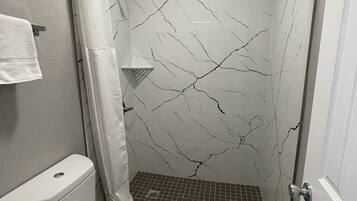 A bathroom with a toilet, a shower with a glass door, and a marble-patterned wall.