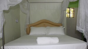 Una cama con dosel, ropa de cama blanca y una toalla enrollada sobre la cama.