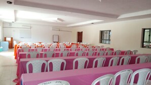 Un salón de conferencias con filas de mesas y sillas, una pizarra y una puerta.