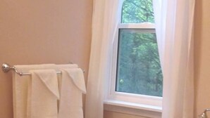 A bathroom with a bathtub, a window with curtains, and a small table with a pitcher. - Chestnut Lane Bed & Breakfast - The Rose Room (New Glasgow)