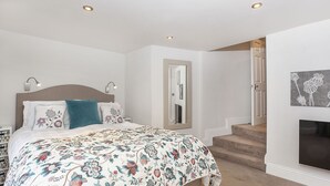 Un dormitorio con cama, lámparas de noche, un espejo, una escalera y una chimenea.