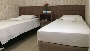 Una habitación de hotel con dos camas individuales, un cabecero de madera, una mesita de noche con un florero y papel tapiz estampado.