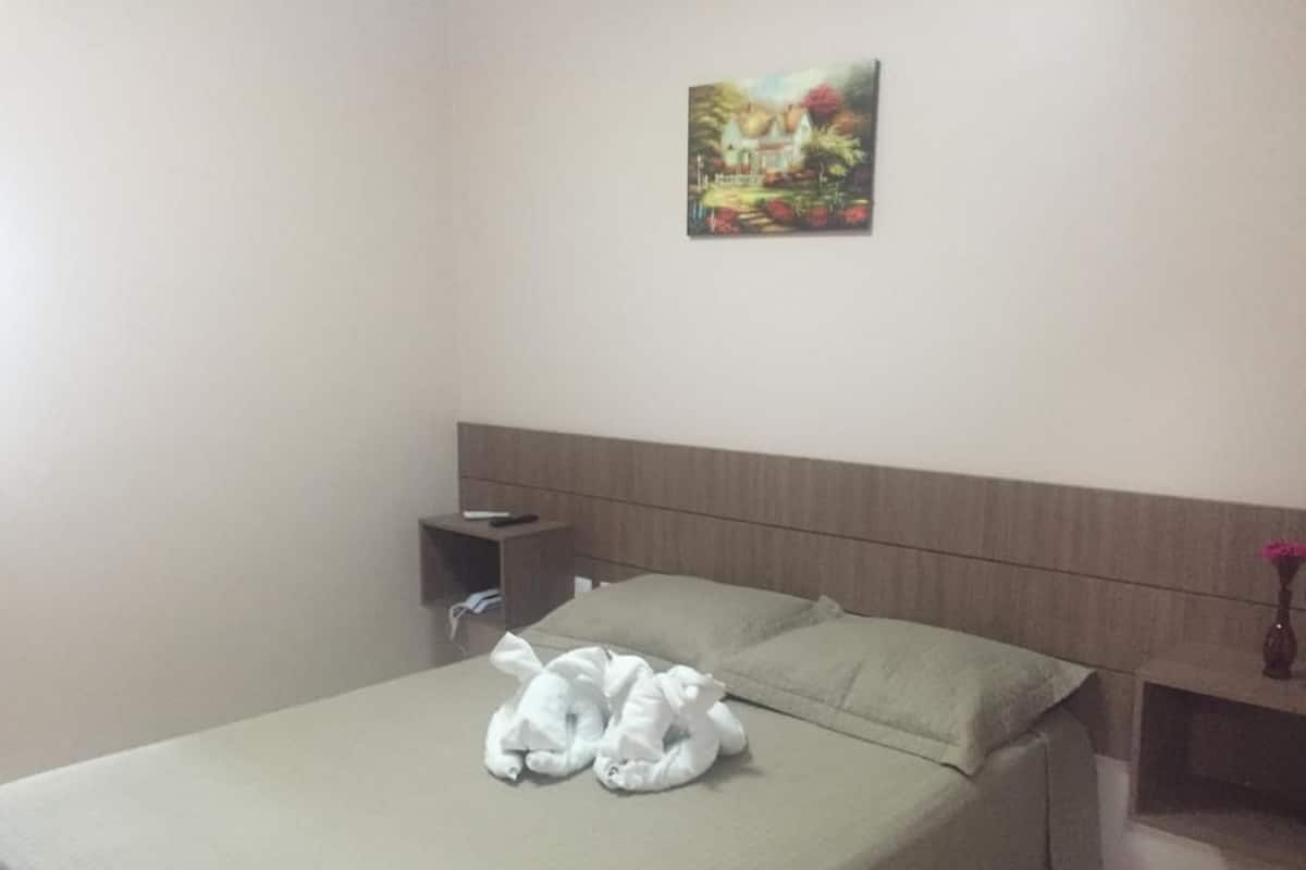 Ein Hotelzimmer mit einem Bett, Kissen, einem Nachttisch, einem Bild an der Wand und einer Vase mit Blumen.