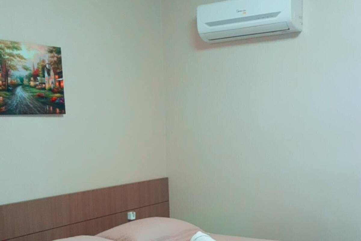Ein Hotelzimmer mit Bett, Kopfteil, Wandklimaanlage und einem Bild an der Wand.