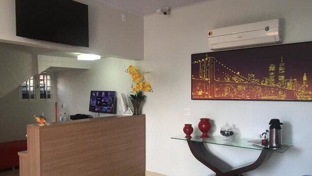 Un área de recepción con un escritorio de madera, una mesa de cristal con adornos y un cuadro de paisaje urbano en la pared.