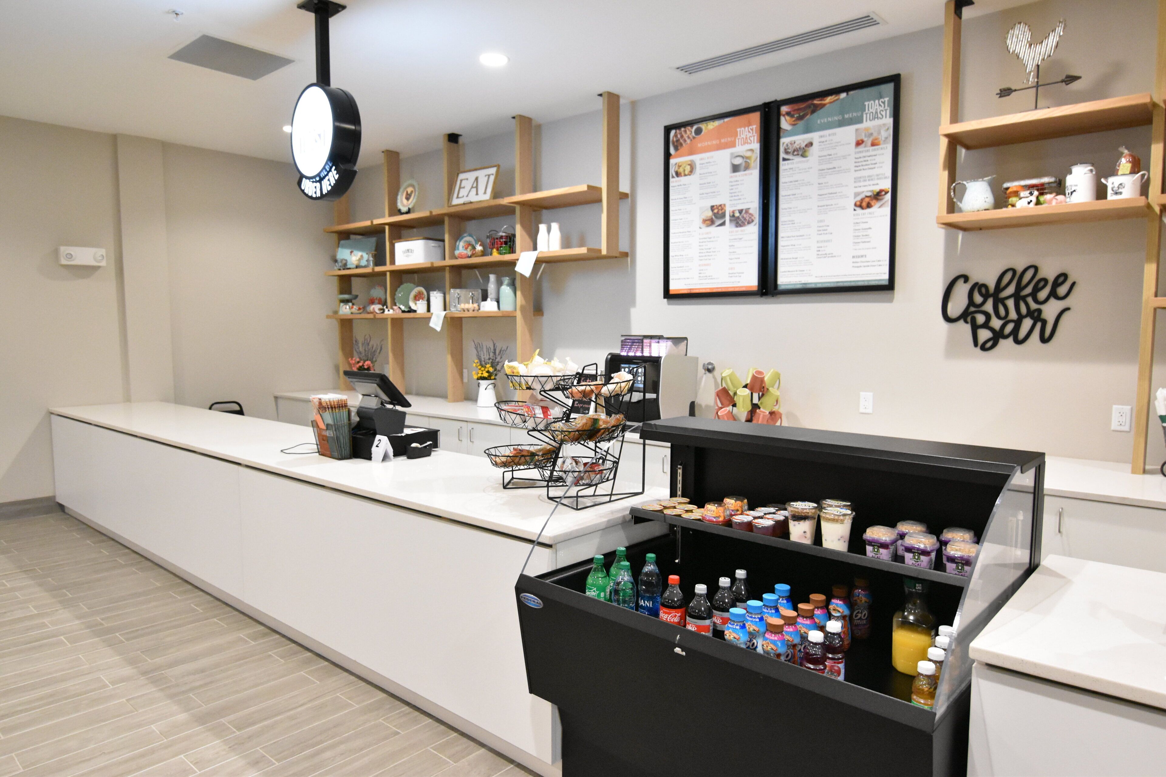 Zona de cafetería con un tablero de menú, una barra y una máquina de café, además de una variedad de bebidas.