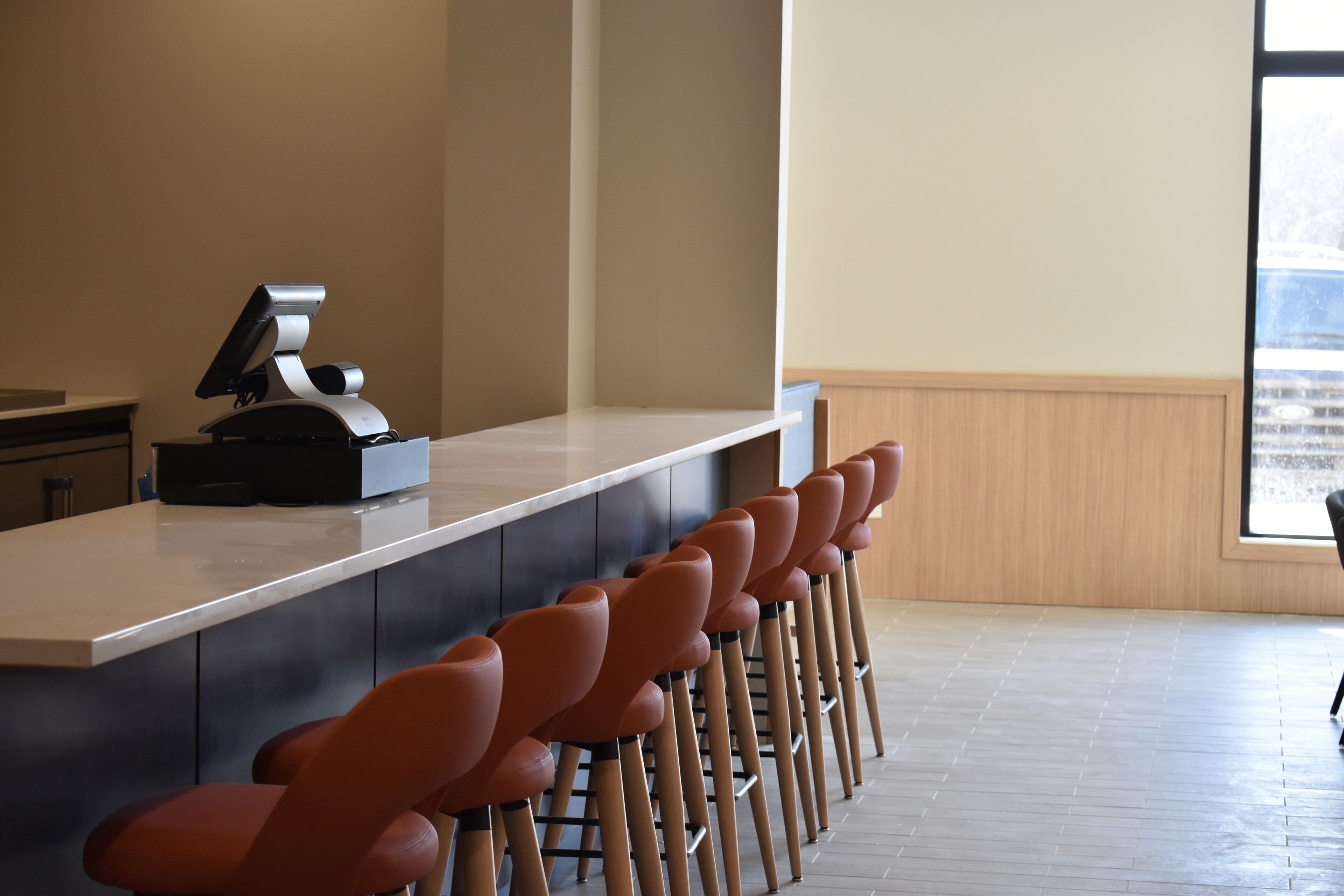 Een bar met een lange toonbank en meerdere oranje barkrukken.
