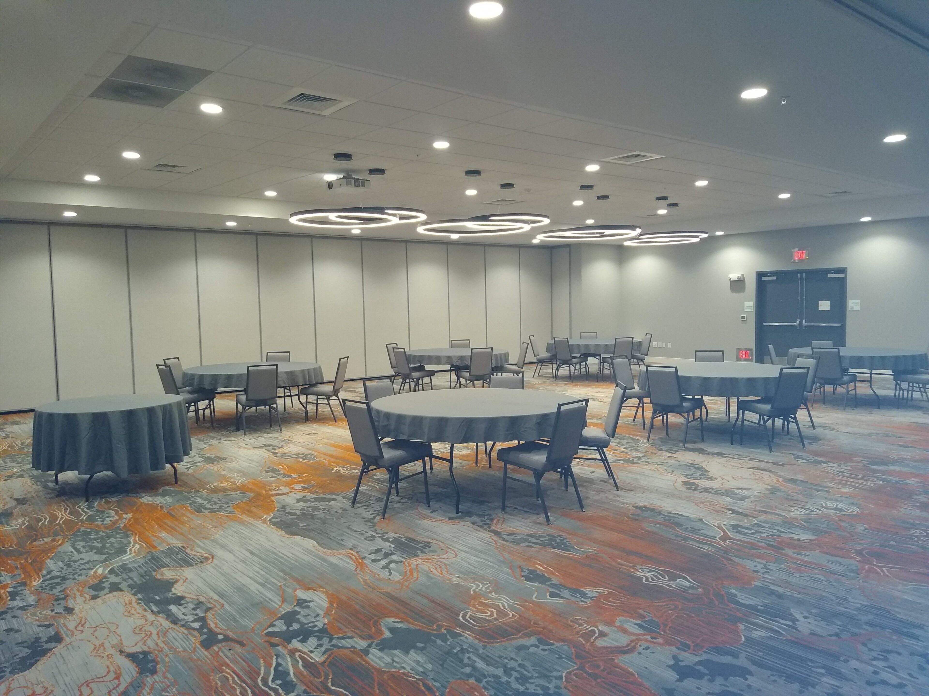 Un salón de conferencias con mesas redondas y sillas, suelo alfombrado e iluminación empotrada en el techo.