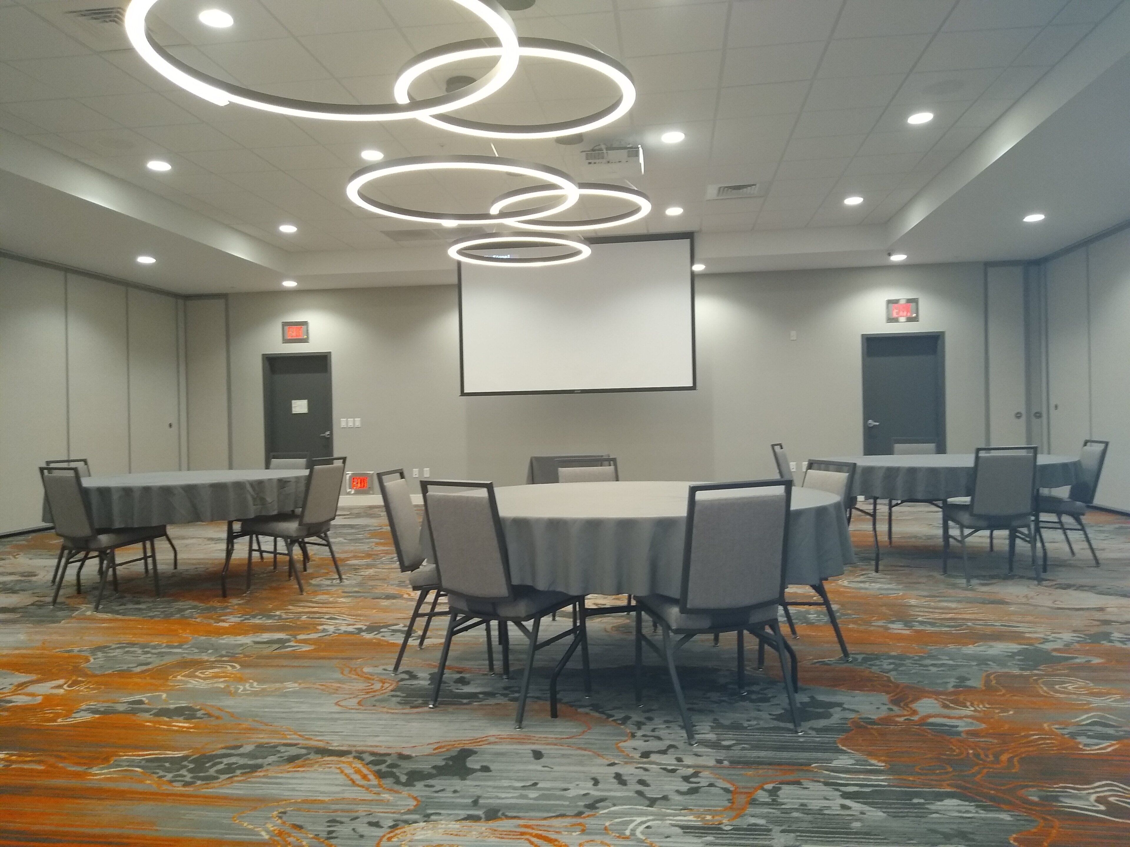 Uma sala de conferências com uma tela grande, várias mesas e cadeiras.