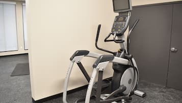 An exercise machine with a digital display, positioned against a wall in a room with a carpeted floor and a door in the background.