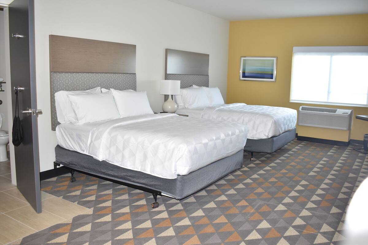 A hotel room with two beds, a bathroom, and a window with a view.