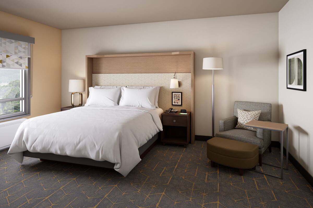 A hotel room with a bed, bedside tables, a chair, a small table, and a lamp.