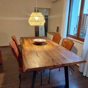 A wooden dining table with chairs, a hanging light fixture, and a window with a view.