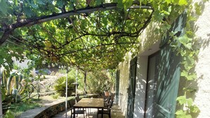 A covered patio with a table and chairs, a stone wall, and greenery.