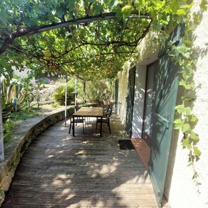 A covered patio with a table and chairs, a stone wall, and greenery.