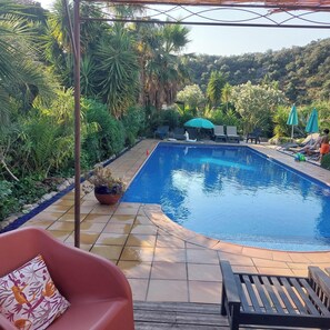 En swimmingpool med ett kaklat poolområde, omgiven av frodig grönska och en pergola.