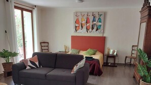 A living room with a sofa, a bed with a red headboard, a colorful rug, and a painting on the wall.