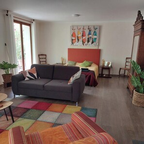 A living room with a sofa, a bed with a red headboard, a colorful rug, and a painting on the wall.
