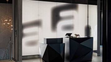 Ein moderner Empfangsbereich mit einer großen LED-Anzeige, die eine Silhouette zeigt, zwei geometrischen schwarzen Podesten und einer Treppe mit Metallgeländer.