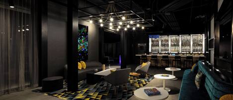 A modern lounge area with a bar, seating, and a large illuminated artwork.