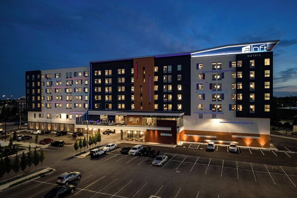 A modern hotel with multiple floors, a parking lot, and a well-lit entrance. - Aloft by Marriott Columbus University District (Columbus)