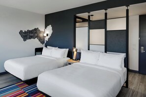 A hotel room with two beds, a modern wall art piece, a nightstand with a lamp, and a colorful striped rug. - Aloft by Marriott Columbus University District (Columbus)
