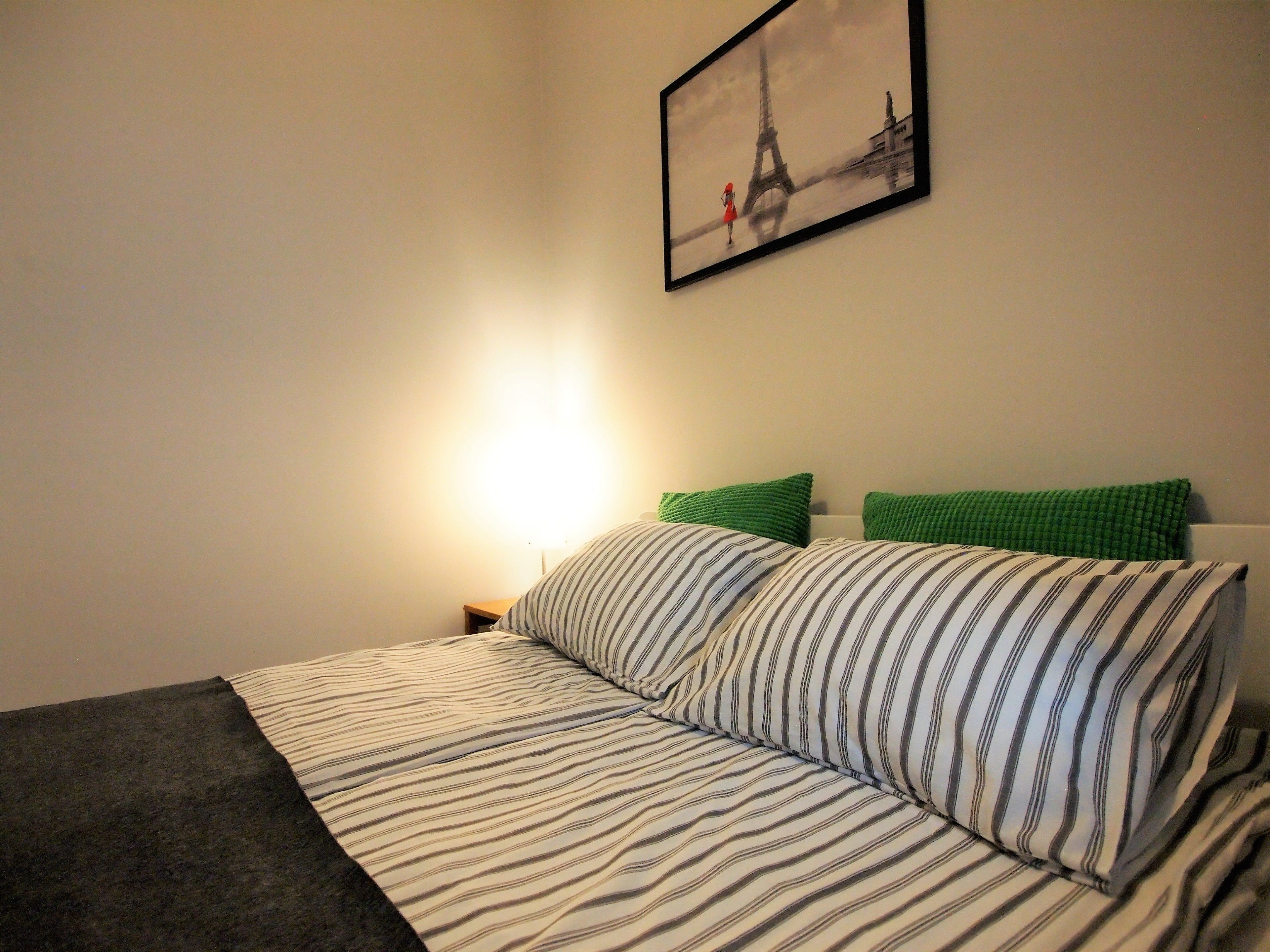 A neatly made bed with striped bedding, a green pillow, and a framed picture of the Eiffel Tower on the wall.