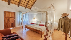 Een slaapkamer met een houten bed, een hemelbed, een etalagepop gekleed in een hoed en shirt, en een rode stoel.