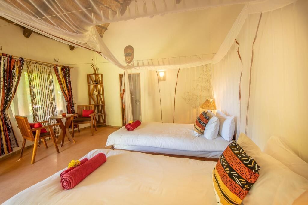 Una habitación con dos camas, una zona de estar con sillas, una mesita y un adorno en la pared.