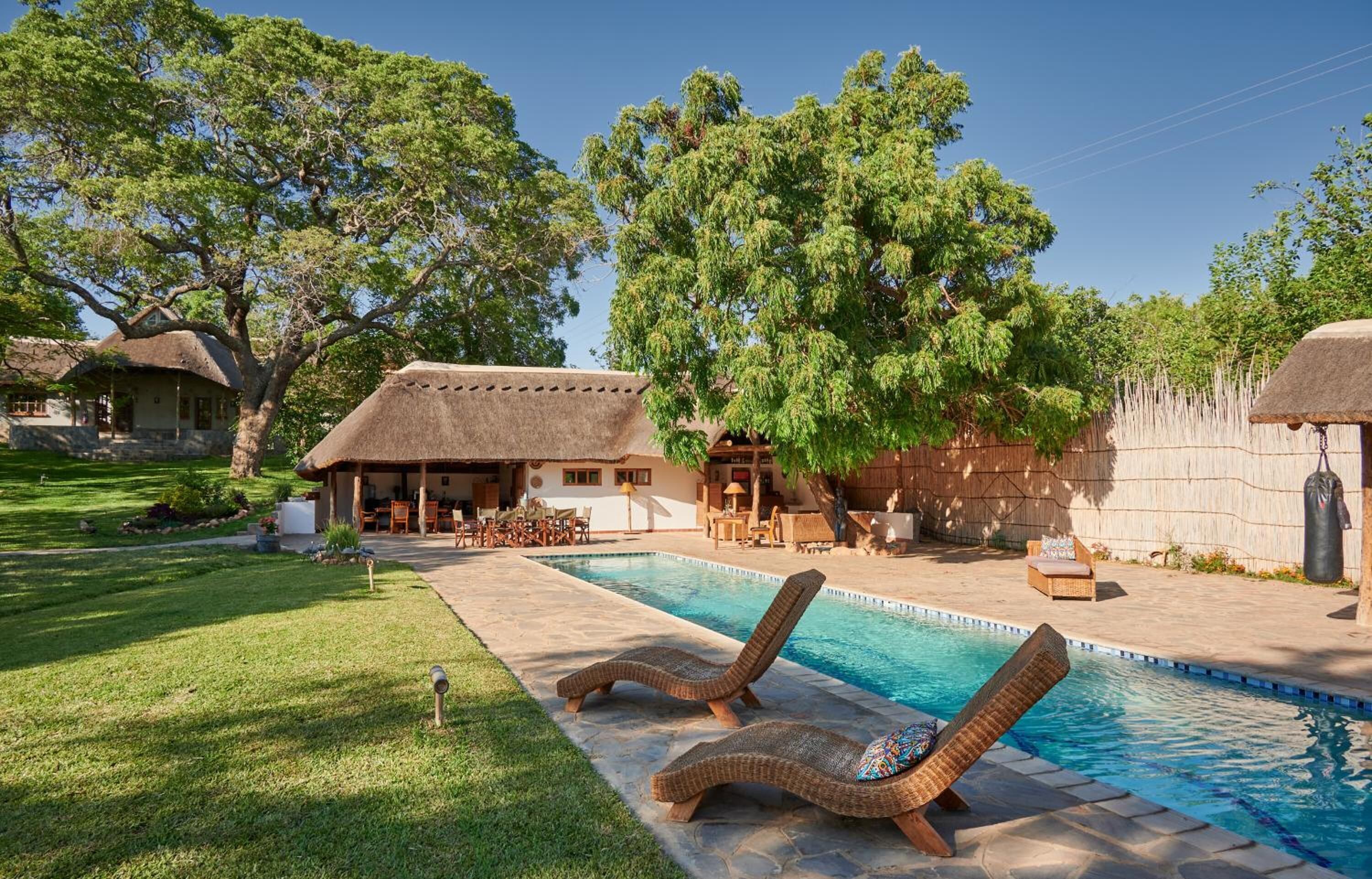A pool area with lounge chairs, a thatched-roof building, and a well-maintained lawn.