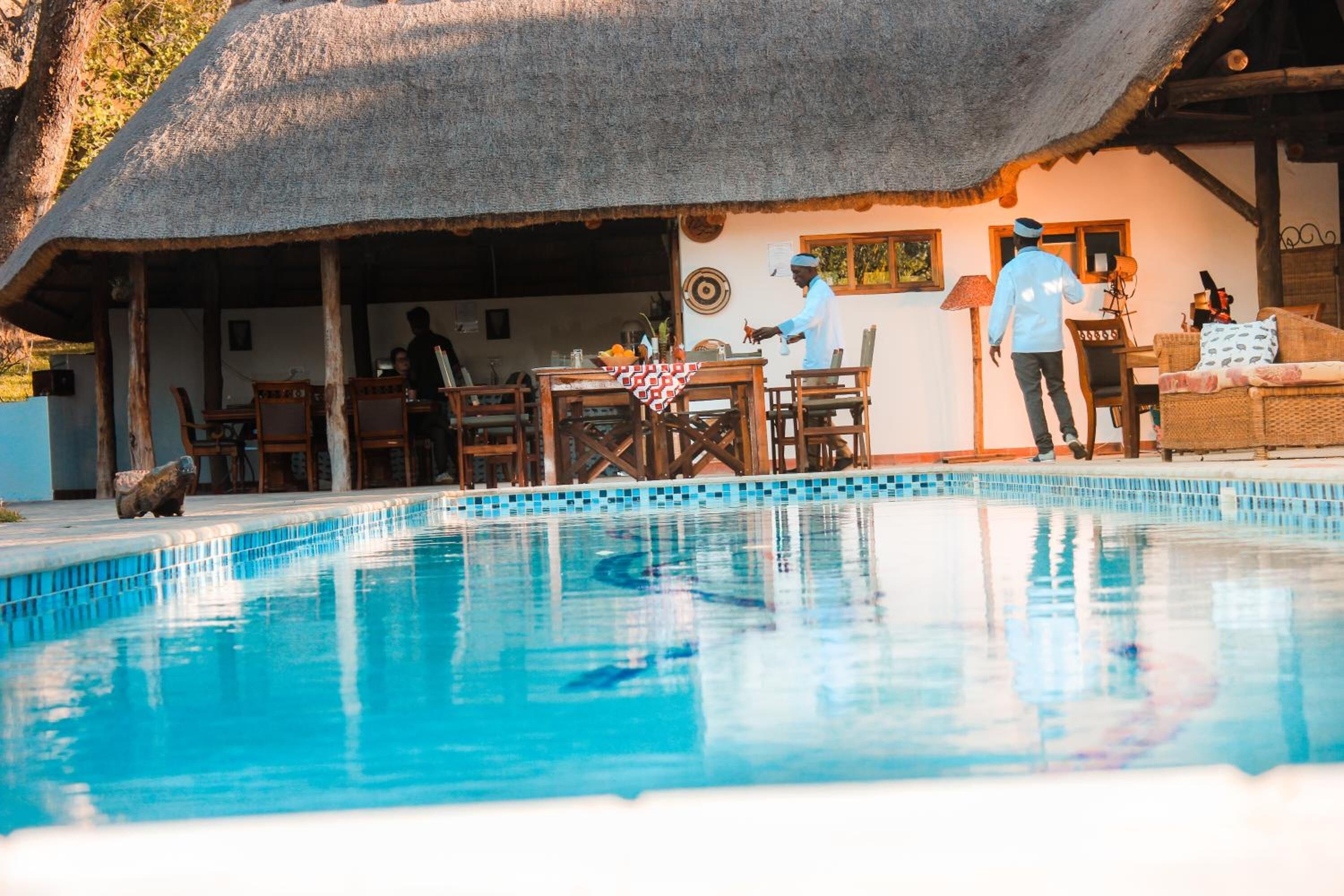 Un espace piscine doté d’un toit de chaume, de mobilier en bois et d’un coin repas.