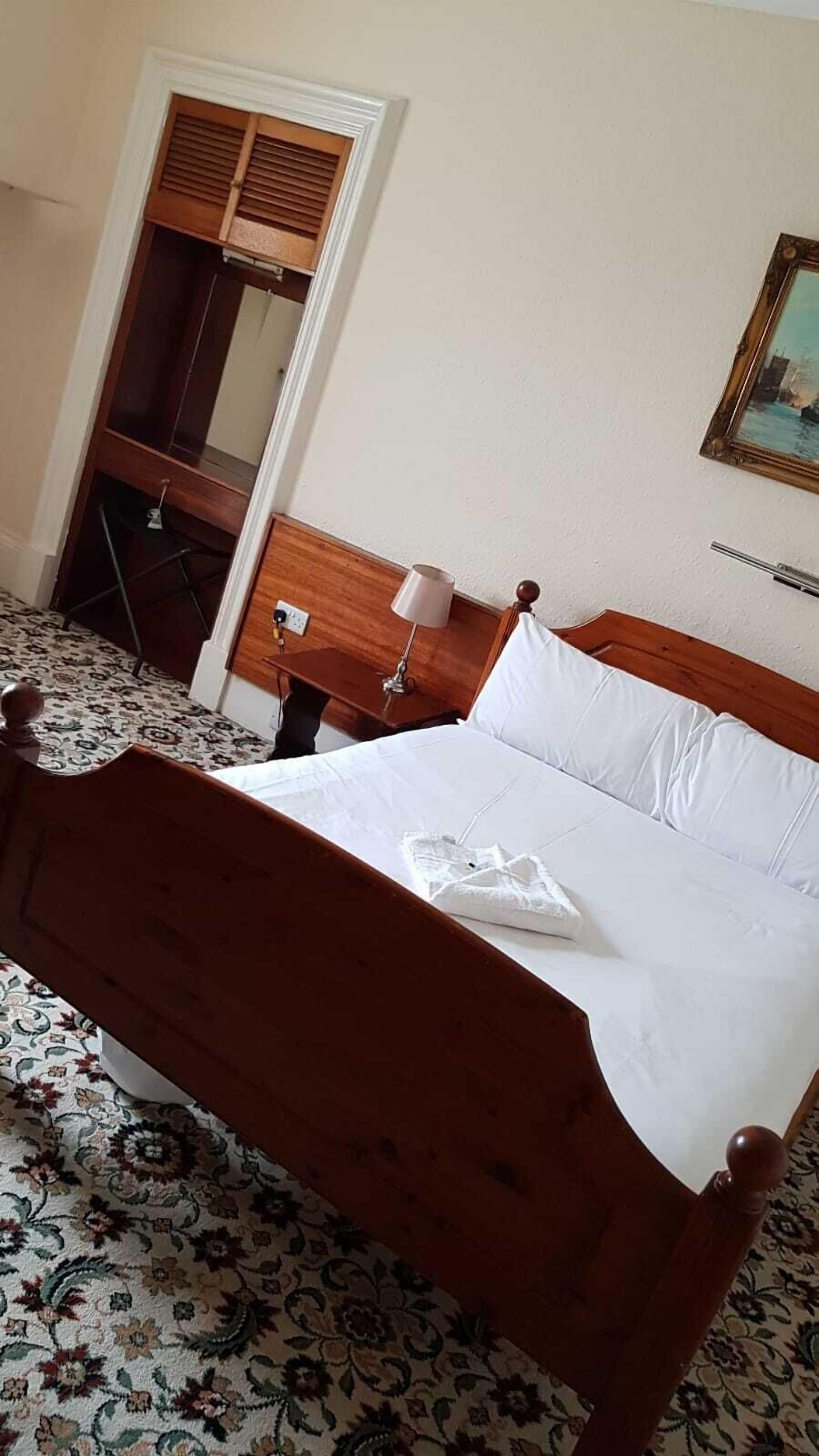 Una cama bien hecha con sábanas blancas, cabecera de madera y mesita de noche con lámpara.