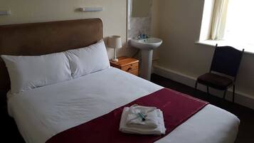 A hotel room with a bed, a nightstand, a sink, and a chair.