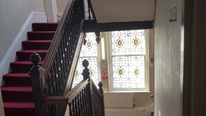 A staircase with red carpeted steps leading to a landing, a black balustrade, and a stained glass window with a 'No Smoking' sign. - LSO GUEST HOUSE  (Dumfries)