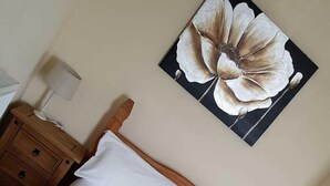A wooden bed with white bedding and a large floral artwork on the wall. - LSO GUEST HOUSE  (Dumfries)