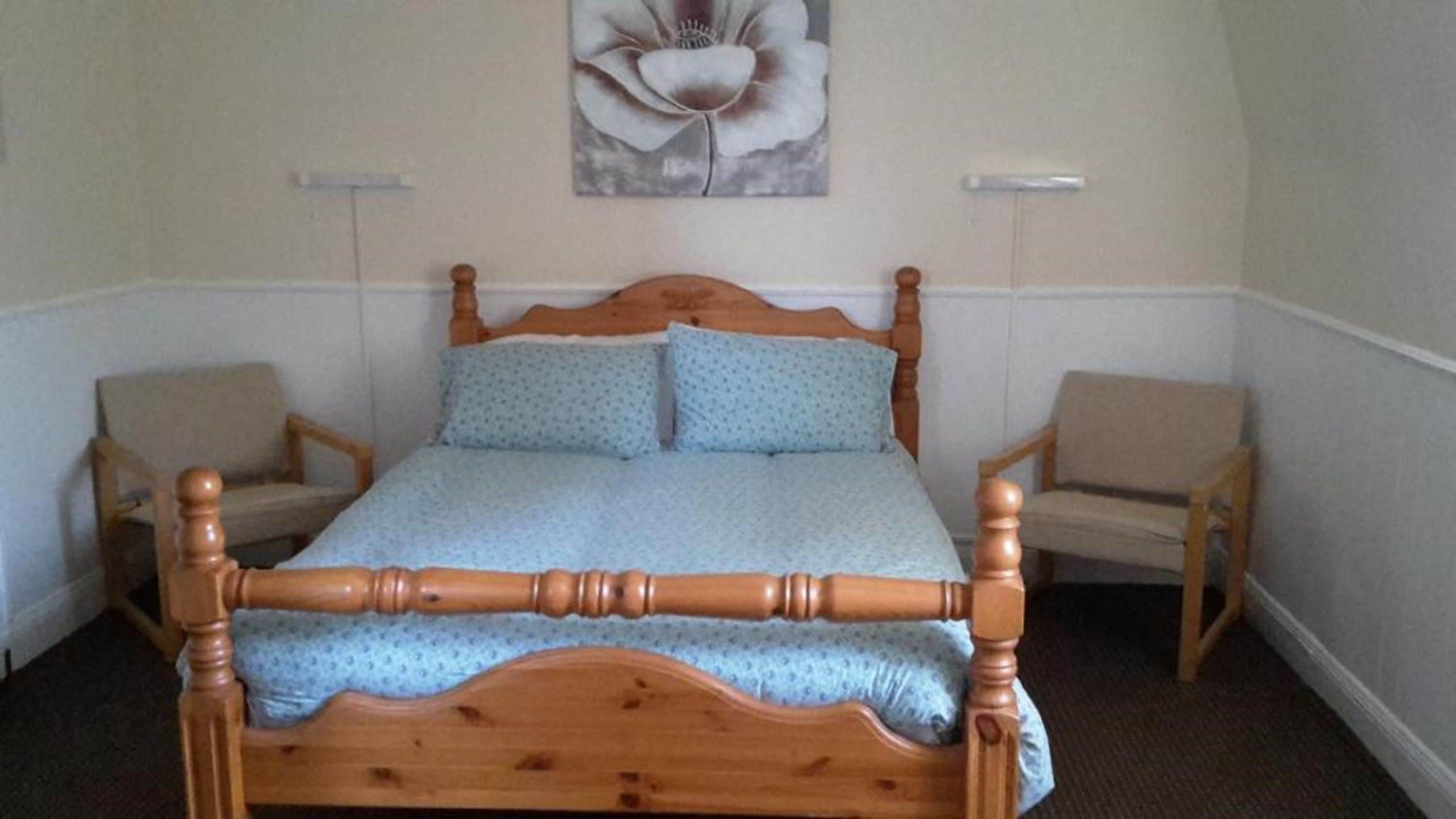 Een slaapkamer met een hemelbed van hout, twee identieke stoelen en een bloemschilderij aan de muur.