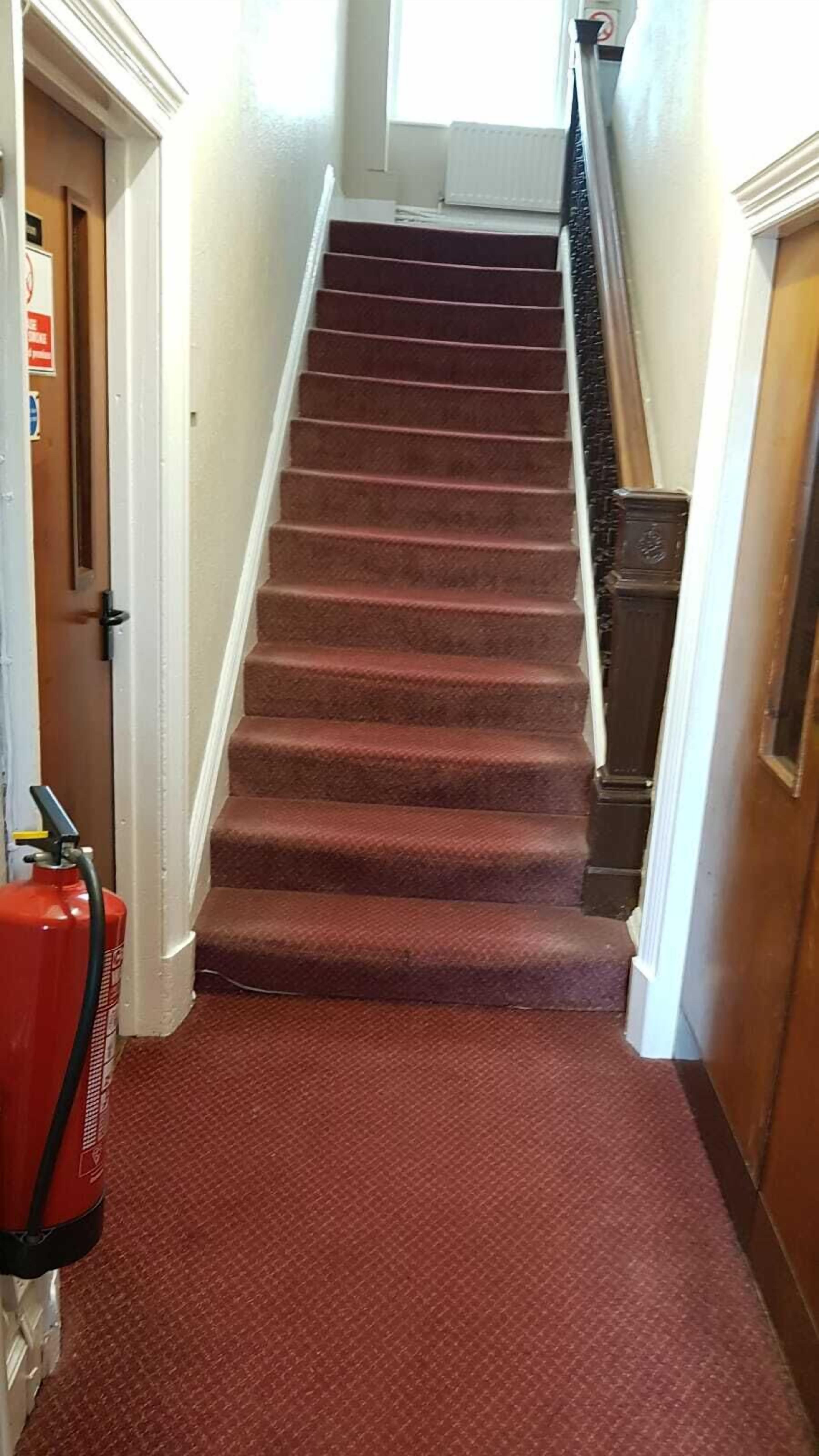 A carpeted staircase with a fire extinguisher on the left.
