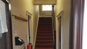 A hallway with a carpeted staircase, a fire exit sign, a telephone, and a fire extinguisher. - LSO GUEST HOUSE  (Dumfries)