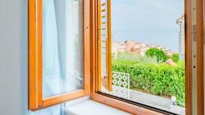 Janela com moldura de madeira e vista para paisagem urbana e vegetação.